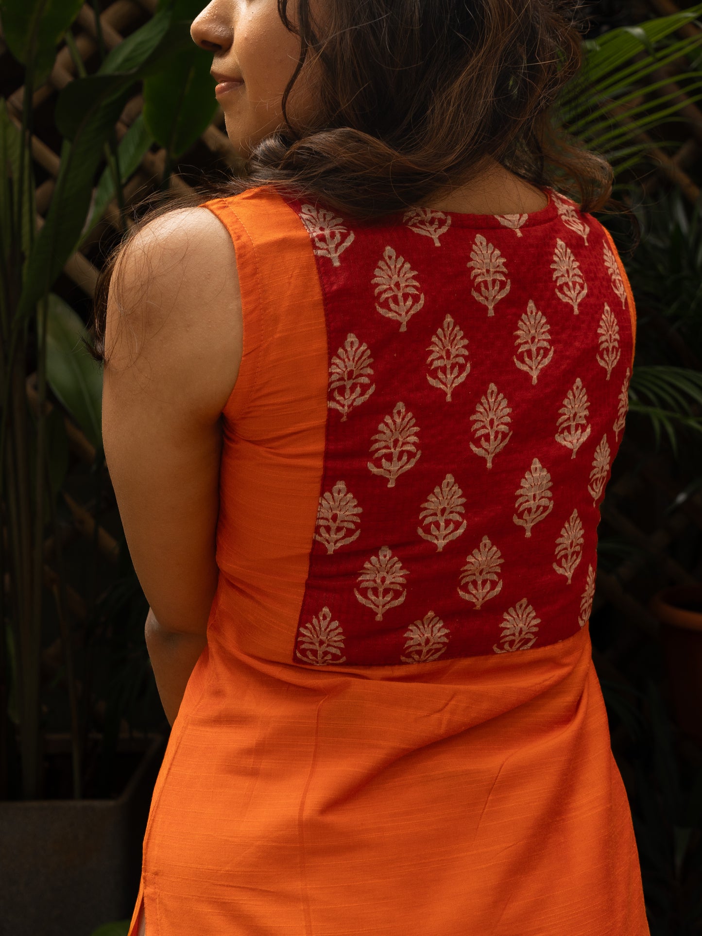 Back mid shot showing the red printed silk square yoke on bright orange dupion kurti, sleeveless, in-house stitched by Sakyaa.