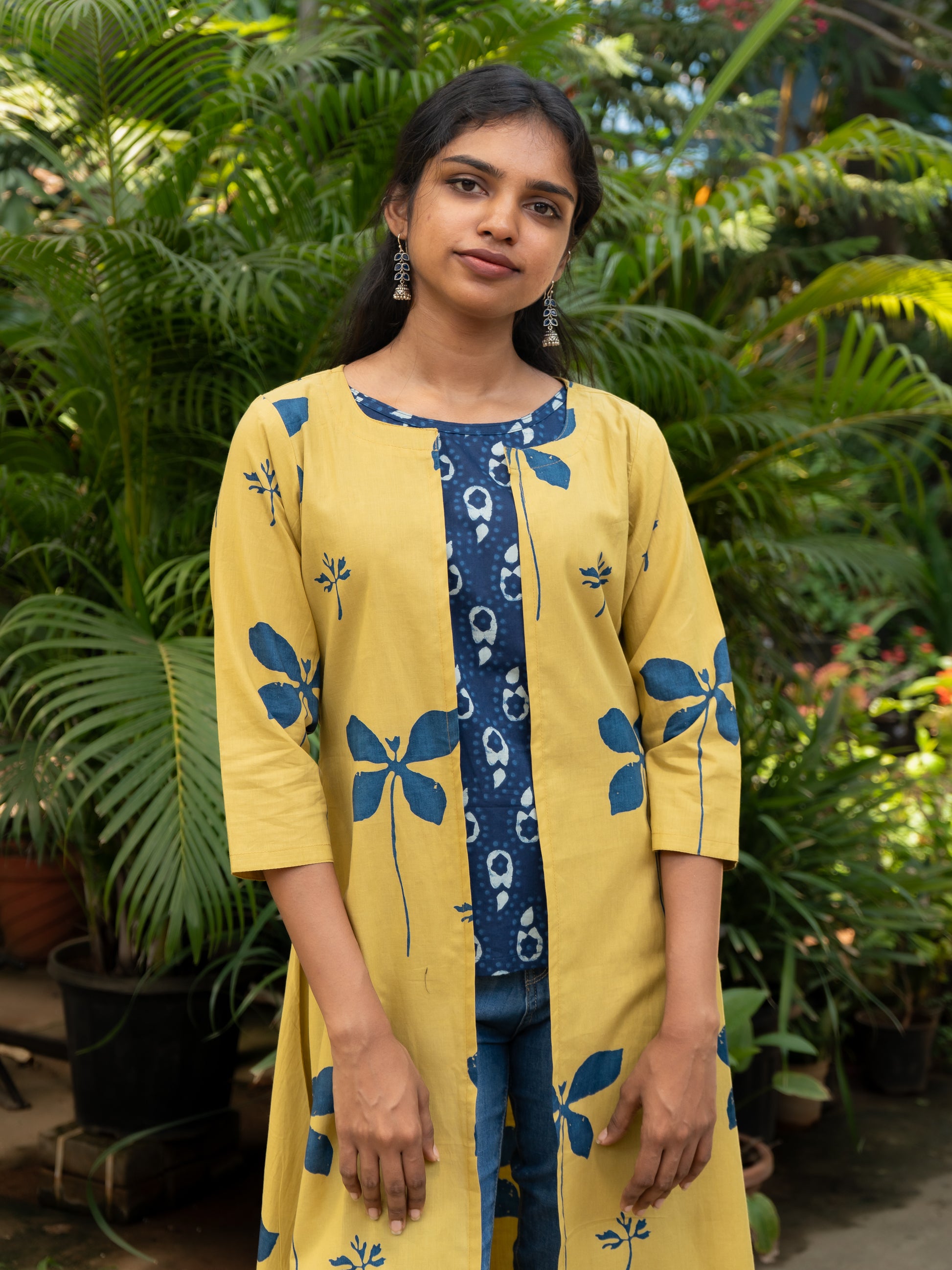 Close-up of yellow cotton cape jacket with bold blue floral prints, open front, and round neck from Sakyaa.