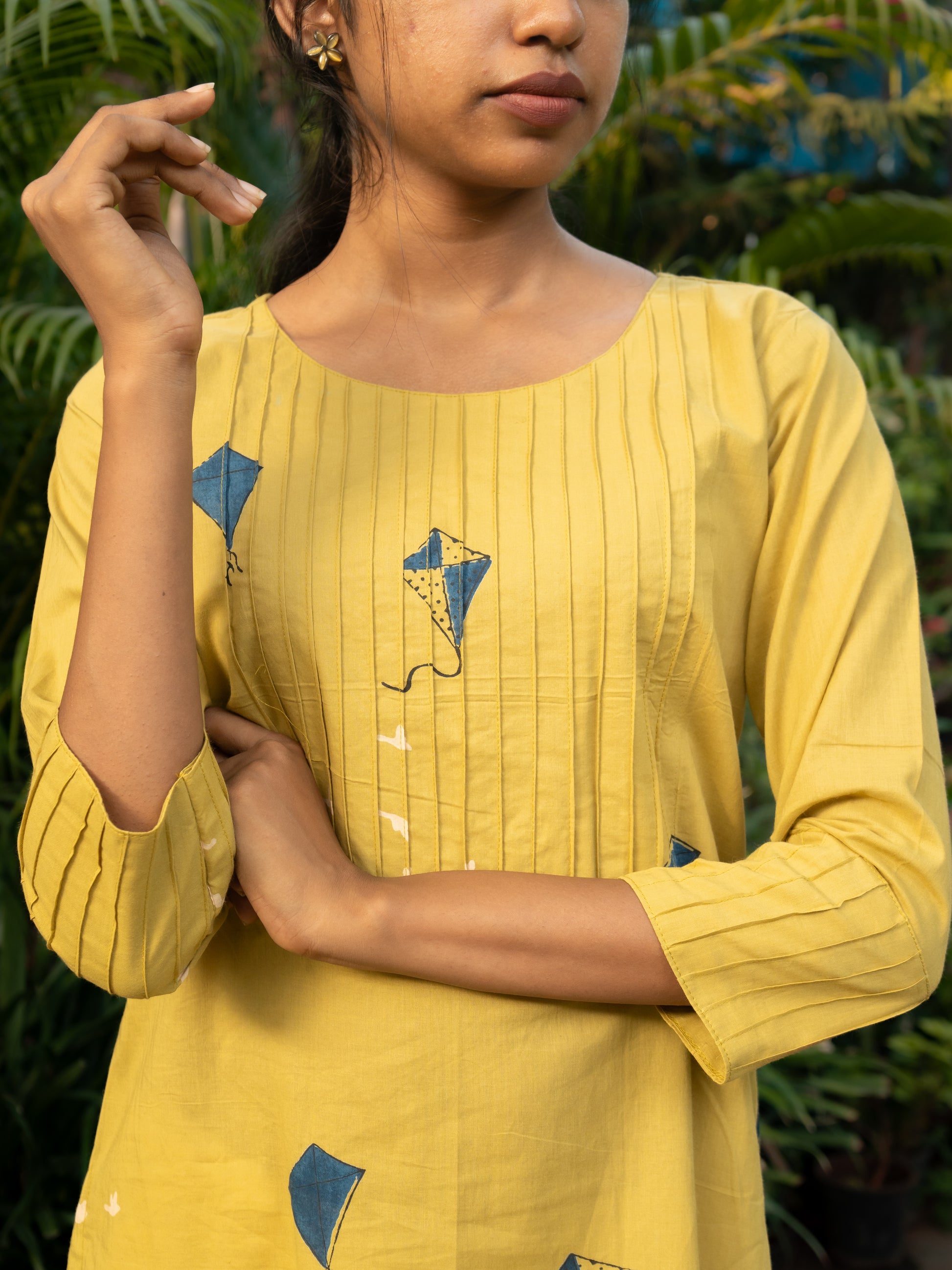 Close-up of pintuck detailing on the yoke and sleeve ends of yellow cotton kurti with blue kite prints