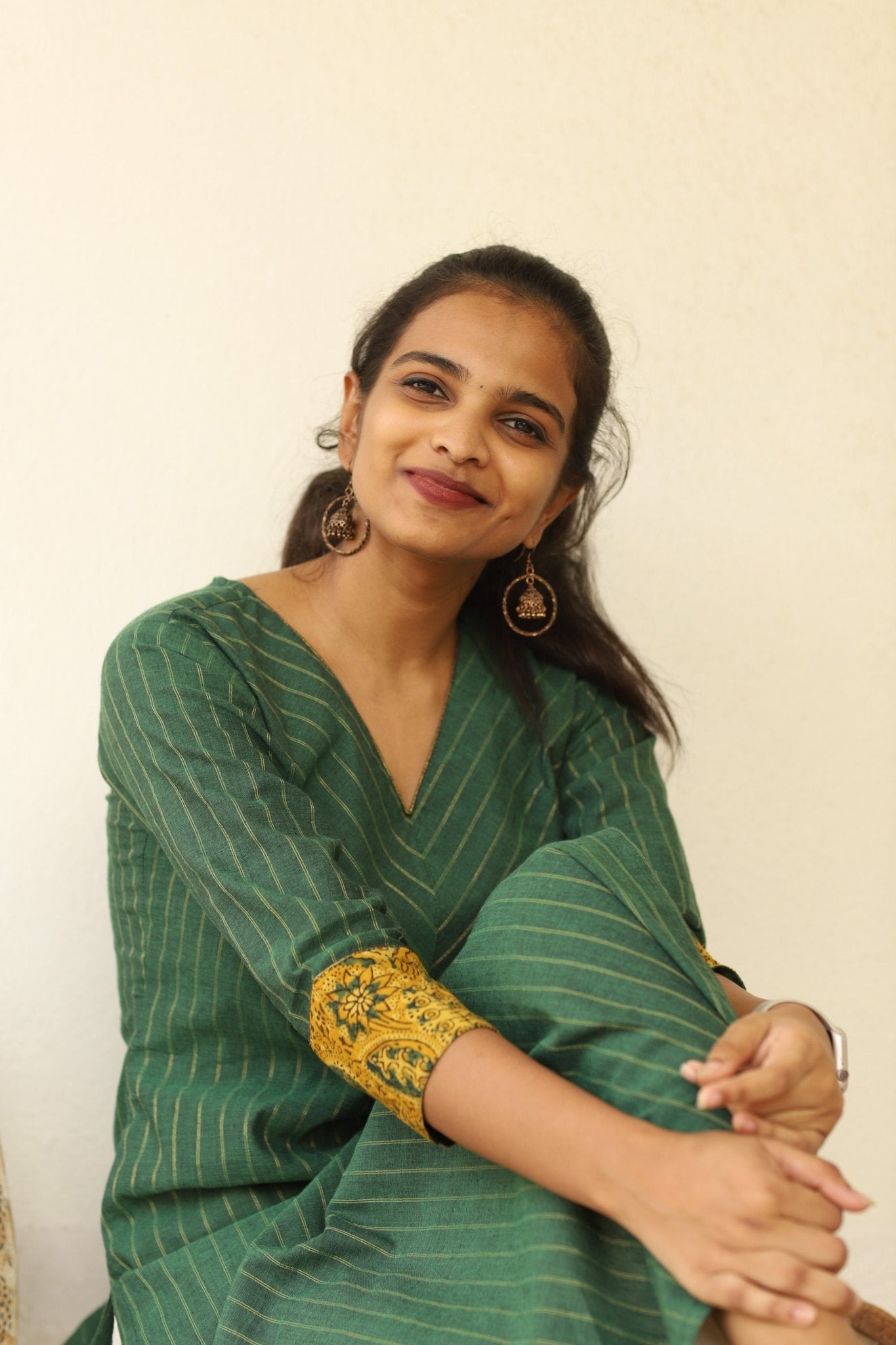 The model is sat posing with a green Kurti with ajrakh detailing