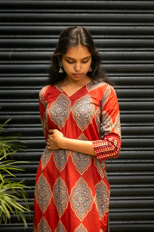 Close-up of a red cotton kurti with V-neckline, featuring intricate blue and white Ajrakh print and shimmering mirror work detailing.