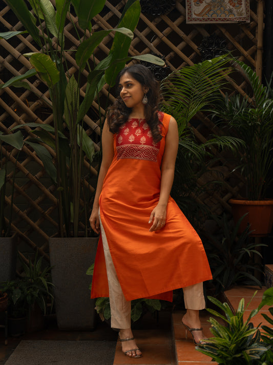 Front full view of bright orange dupion silk kurti with red printed silk square yoke, round neck with self button, sleeveless, in-house stitched by Sakyaa.