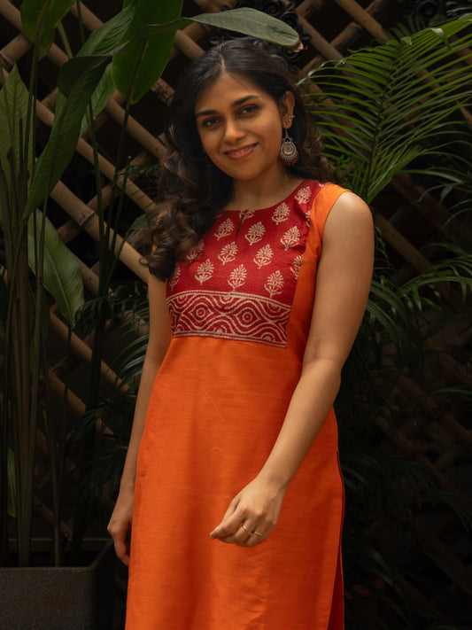 Mid shot highlighting the round neckline with self button and red printed silk square yoke on an orange dupion kurti, sleeveless, handcrafted in-house.